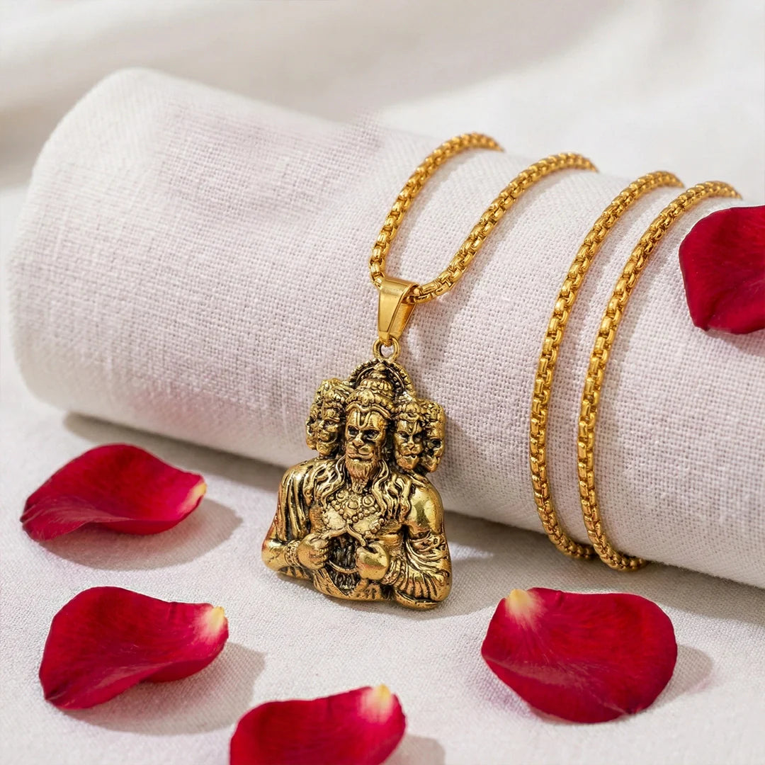 Gold necklace with a pendant on a white fabric background with red petals